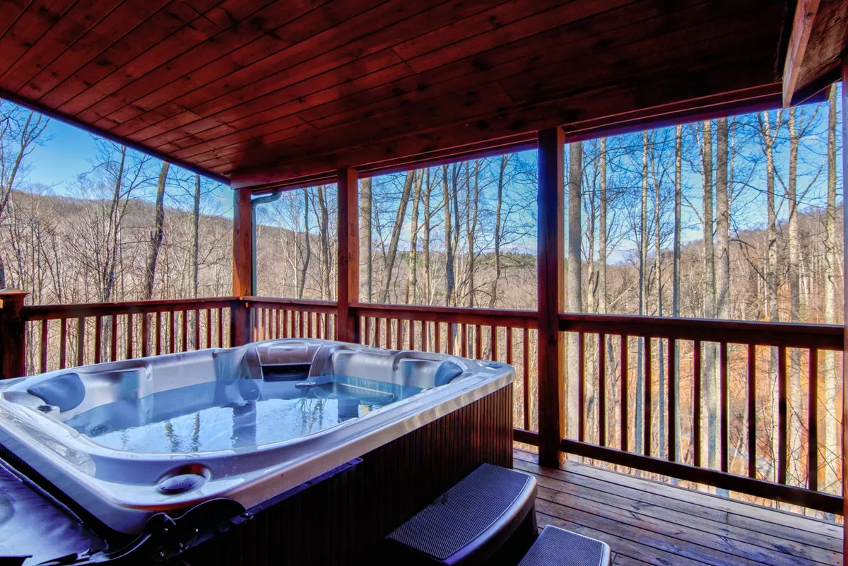 A serene exterior shot of the cabin's hot tub nestled on a wooden deck. The hot tub features a wooden railing and is surrounded by lush green trees, providing privacy and a tranquil atmosphere. The scenic view beyond the deck immerses you in the peaceful woods, aligning perfectly with the section's emphasis on nature and relaxation.