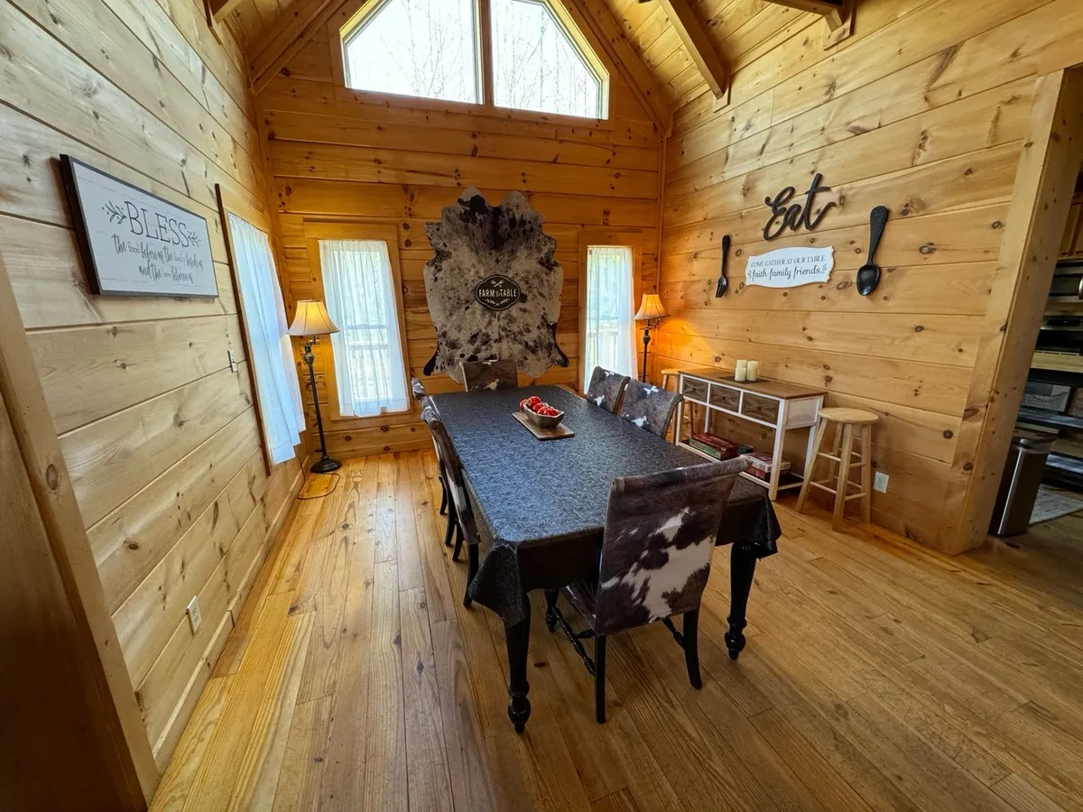 This image features a spacious, rustic dining area with a long wooden table, cowhide decor, and wood-paneled walls. The table is set for a gathering, with festive signage and a cozy, inviting atmosphere ideal for group meals and celebrations.