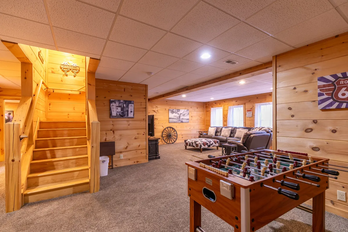 This image showcases a comfortable lounge area featuring a foosball table, a large, inviting sectional sofa, a wooden staircase, wall decor, and a television. The space is arranged for both relaxation and entertainment, enabling group activities like foosball and movie watching.