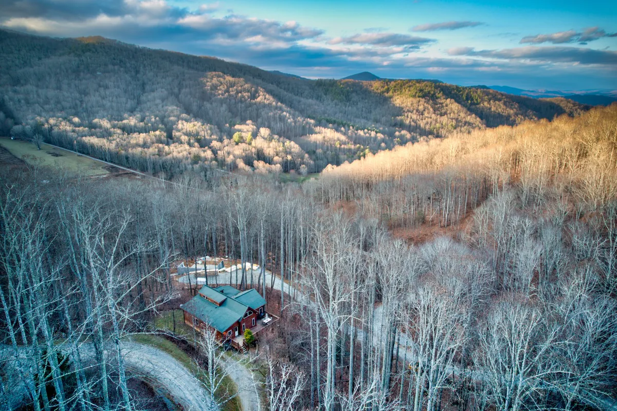A picturesque log cabin nestled among vibrant autumn trees, set at the end of a winding road in a peaceful, gated mountain community. The serene natural surroundings invite outdoor exploration and quiet moments under a vast, starlit sky.