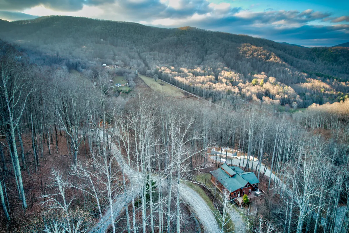 A broad view of the house, set against a backdrop of winding roads, dense trees, and distant mountains. The perspective showcases the tranquility of the setting and hints at hiking, nature walks, and wildlife exploration just moments away.
