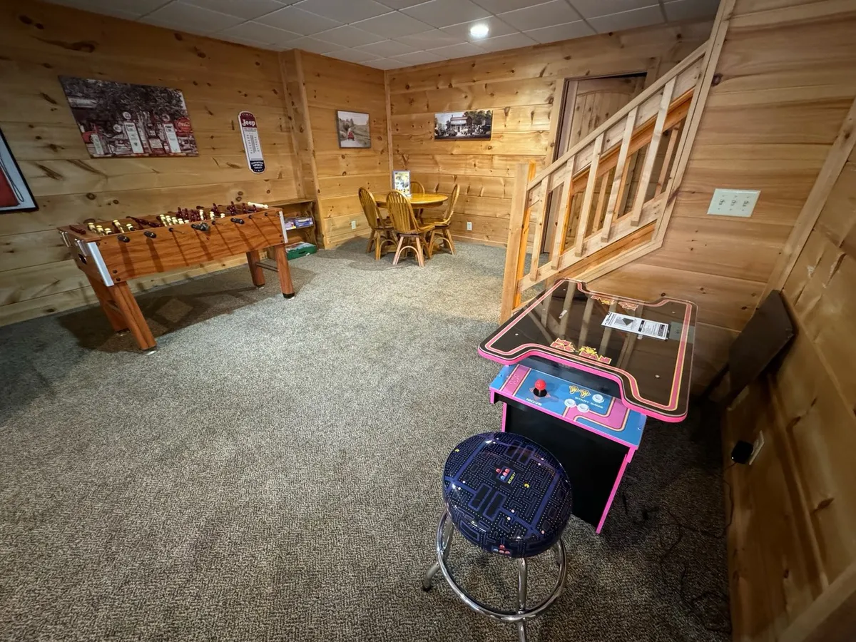 A lively corner of the lower level, this image features both a foosball table and a classic arcade game, as well as a dining table for group activities or snacks between games. The mood is playful and relaxed, perfect for all ages.